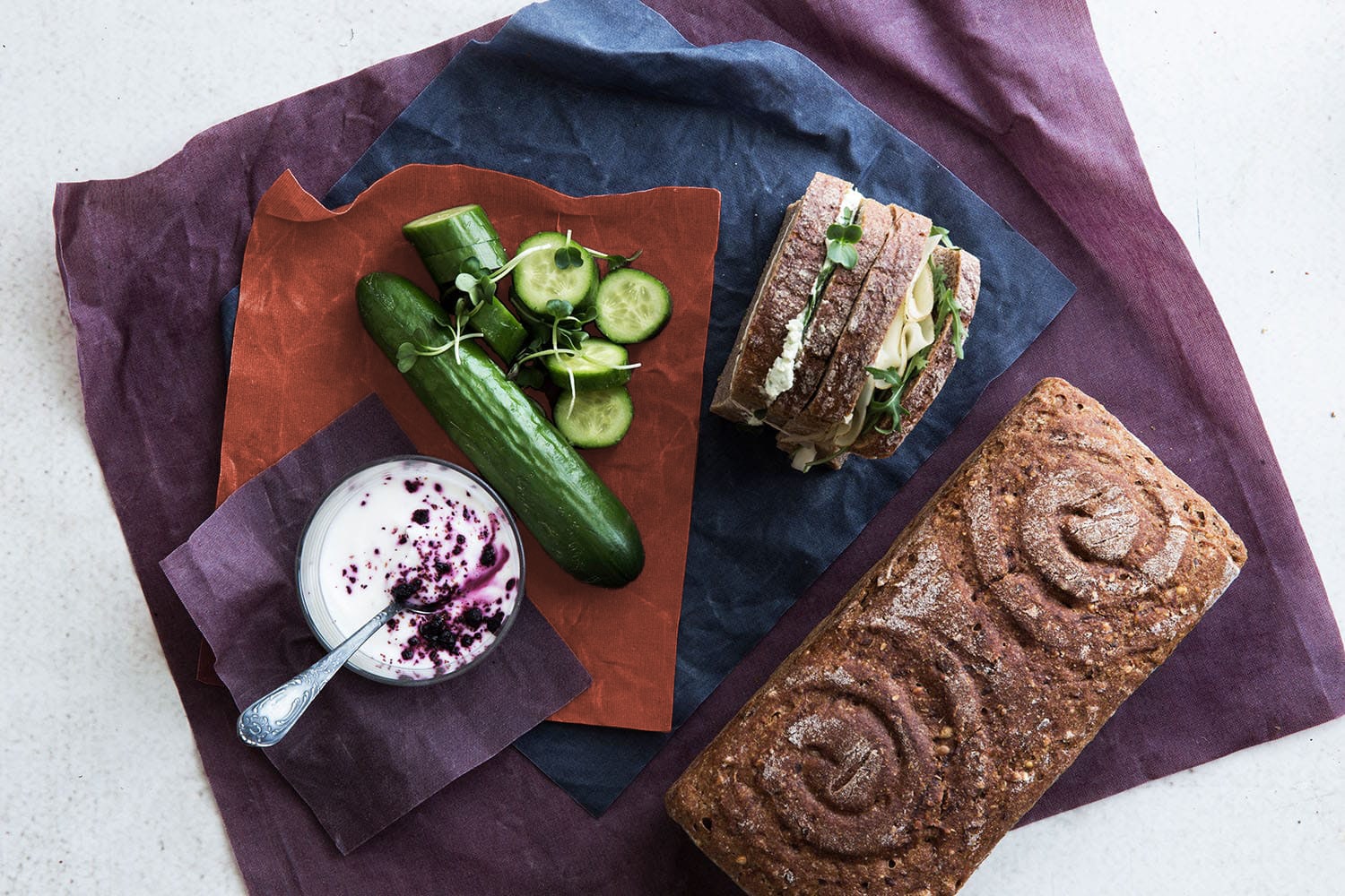 Ein Glas, eine Gurke und eine Schnitte sowie ein Brot liegen auf Bienenwachstücher